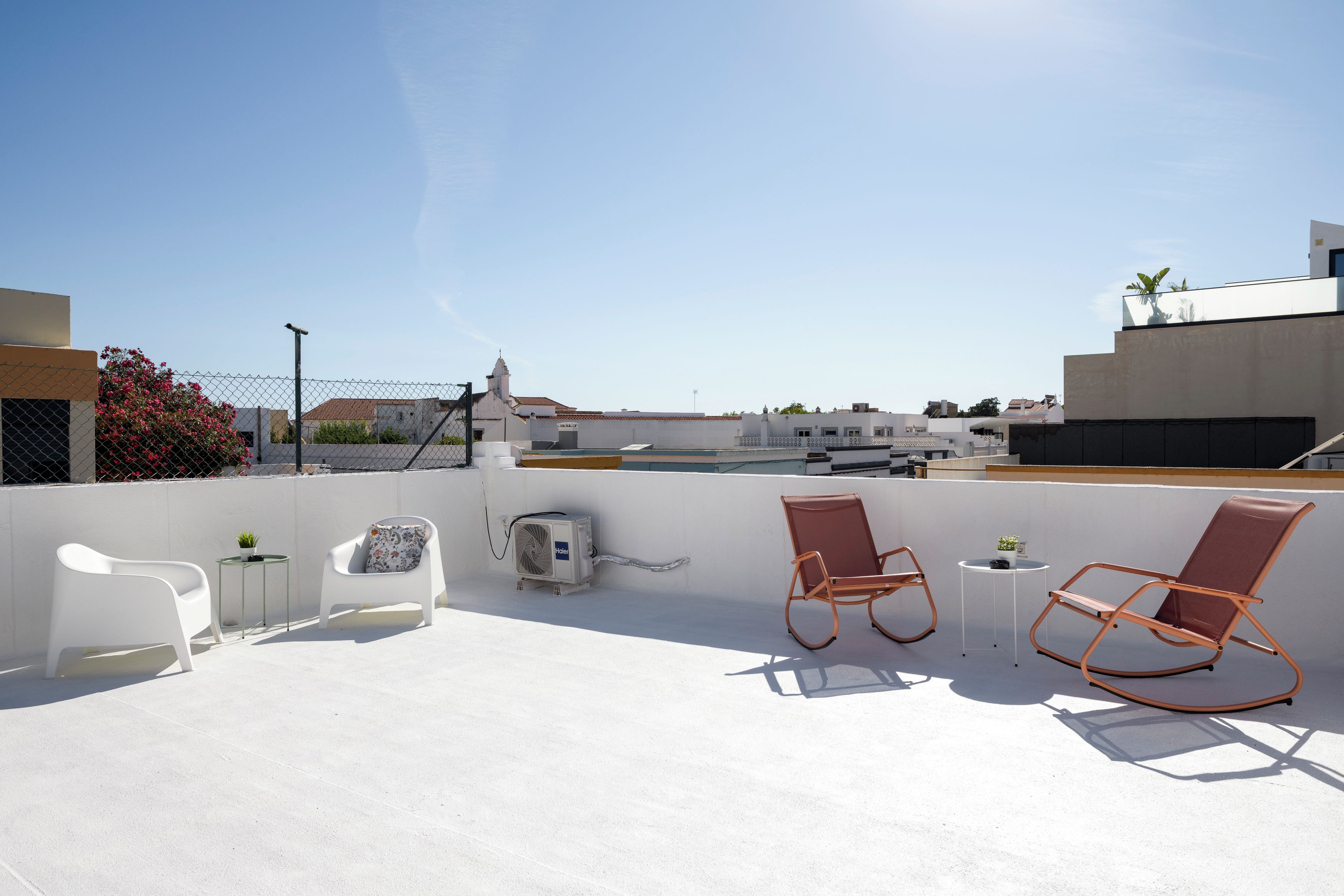 A rooftop terrace with two rocking chairs, a small table, and an air conditioning unit.