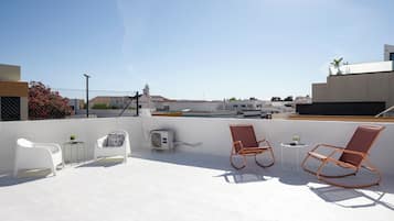 A rooftop terrace with two rocking chairs, a small table, and an air conditioning unit.