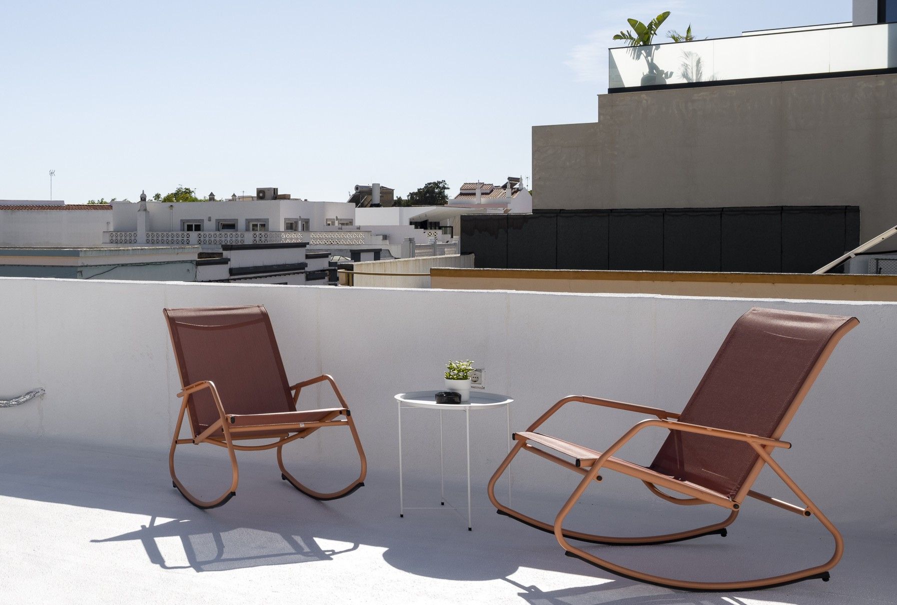 Deux fauteuils à bascule sur une terrasse en toit-terrasse, avec une petite table et un pot de fleurs.