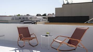Deux fauteuils à bascule sur une terrasse en toit-terrasse, avec une petite table et un pot de fleurs.