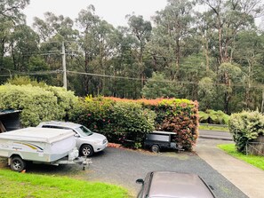 A campsite with a white camper van and a trailer, surrounded by dense greenery and trees. - Puffing Billy Guesthouse: 
Escape the suburbs and enjoy the Dandenong Ranges! (Cockatoo)
