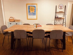 A dining area with a wooden table, grey chairs, a framed sunflower artwork, a shelf with books, and a clock on the wall. - Puffing Billy Guesthouse: 
Escape the suburbs and enjoy the Dandenong Ranges! (Cockatoo)