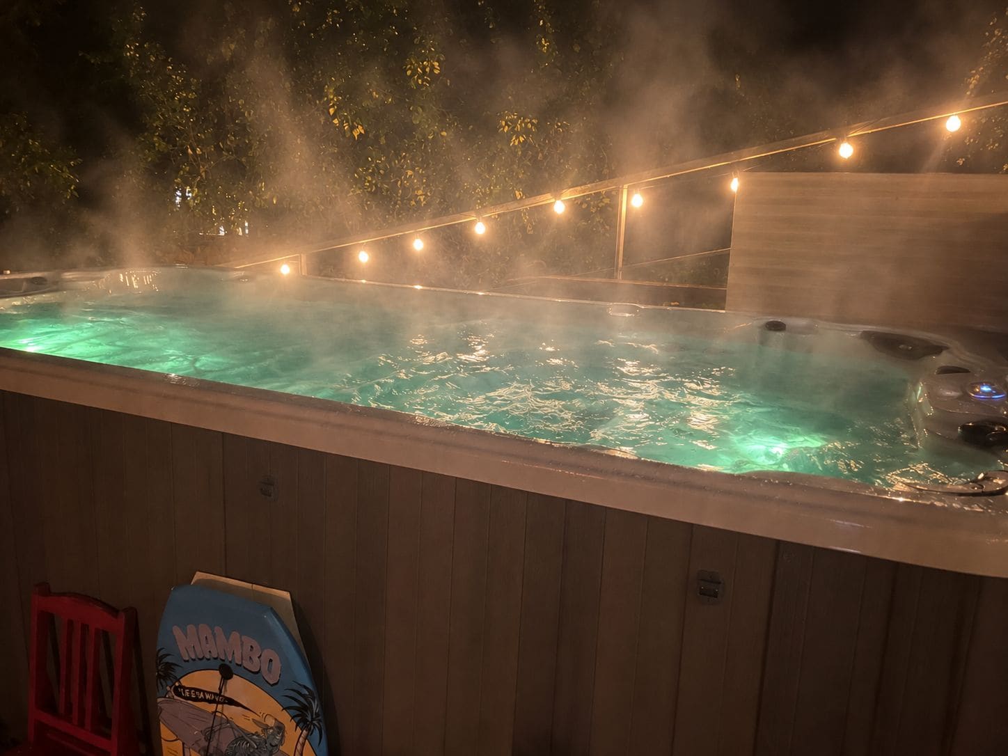 A hot tub with a misty atmosphere, surrounded by string lights and a wooden deck.