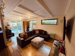 A living room with a sofa, ottoman, and a television. There is a window with a view of greenery outside. - Puffing Billy Guesthouse: 
Escape the suburbs and enjoy the Dandenong Ranges! (Cockatoo)