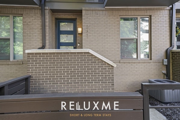 A building with a brick facade, a dark blue door, and a sign that reads 'RELLUXME SHORT & LONG TERM STAYS'.