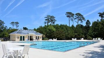 A swimming pool with lounge chairs and a small building, surrounded by trees.