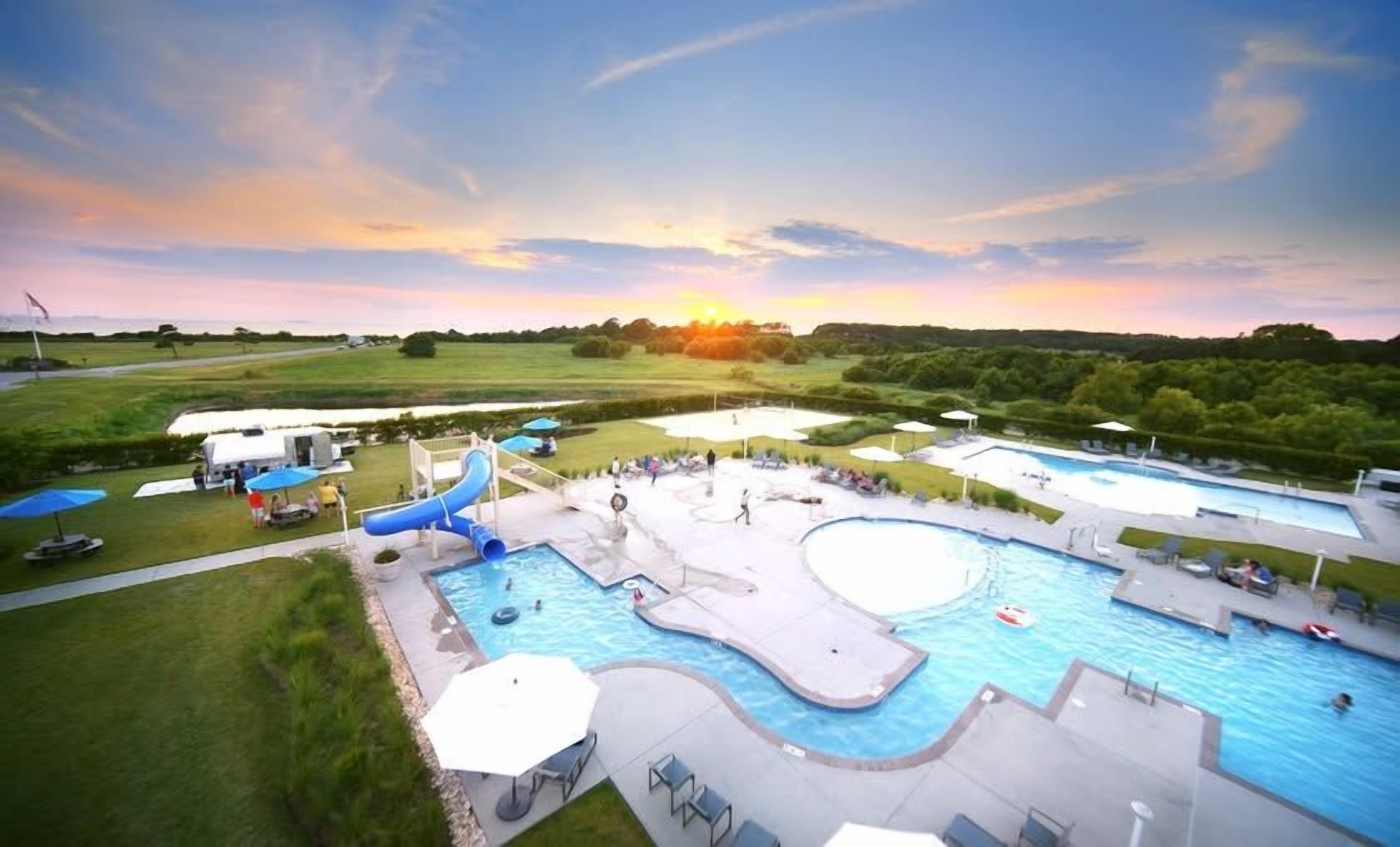 Resort-style pools, waterslide, and sunset views over open countryside