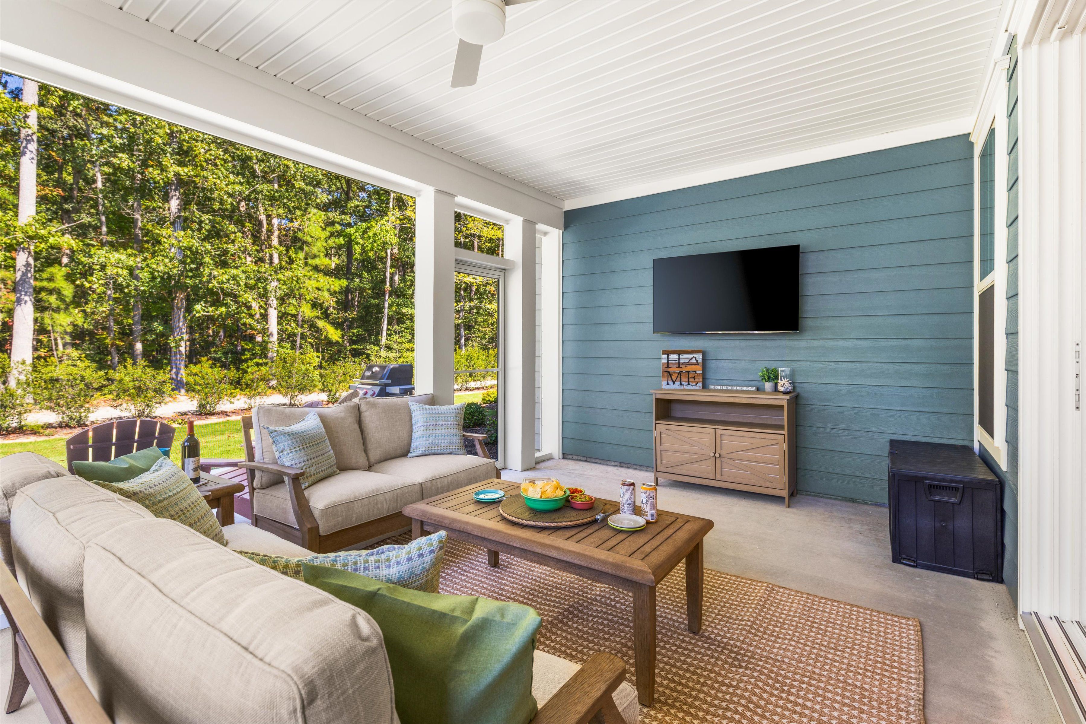 Covered outdoor lounge with TV, comfy seating, and peaceful wooded views
