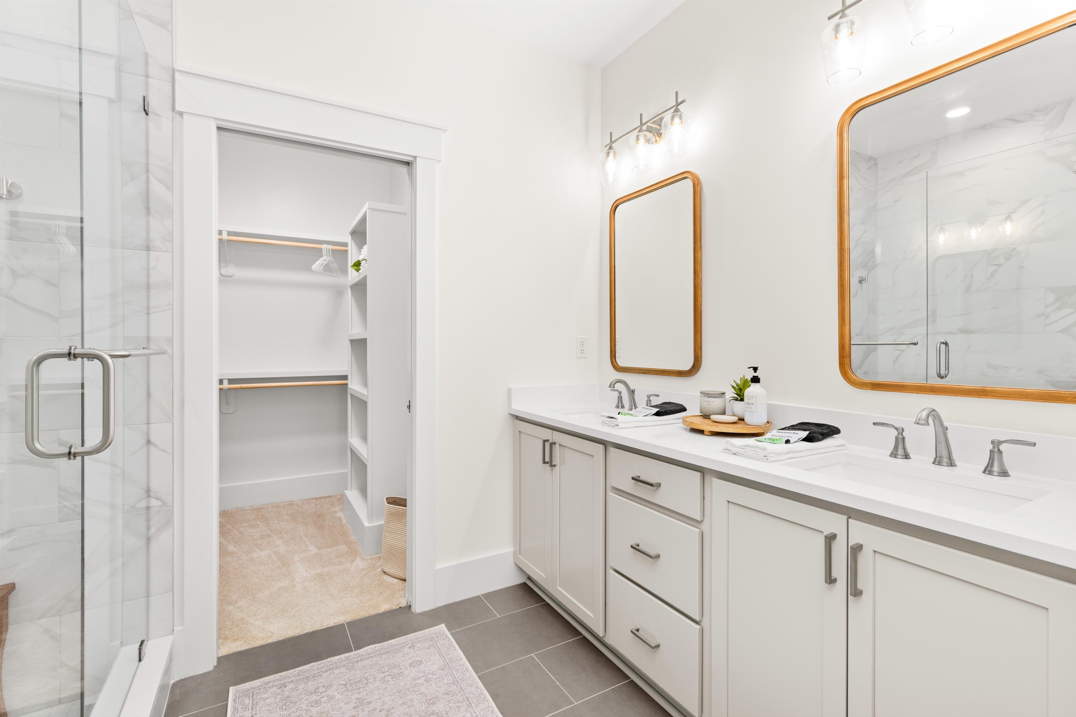 Bright spa-like bath with double vanity, glass shower, and walk-in closet