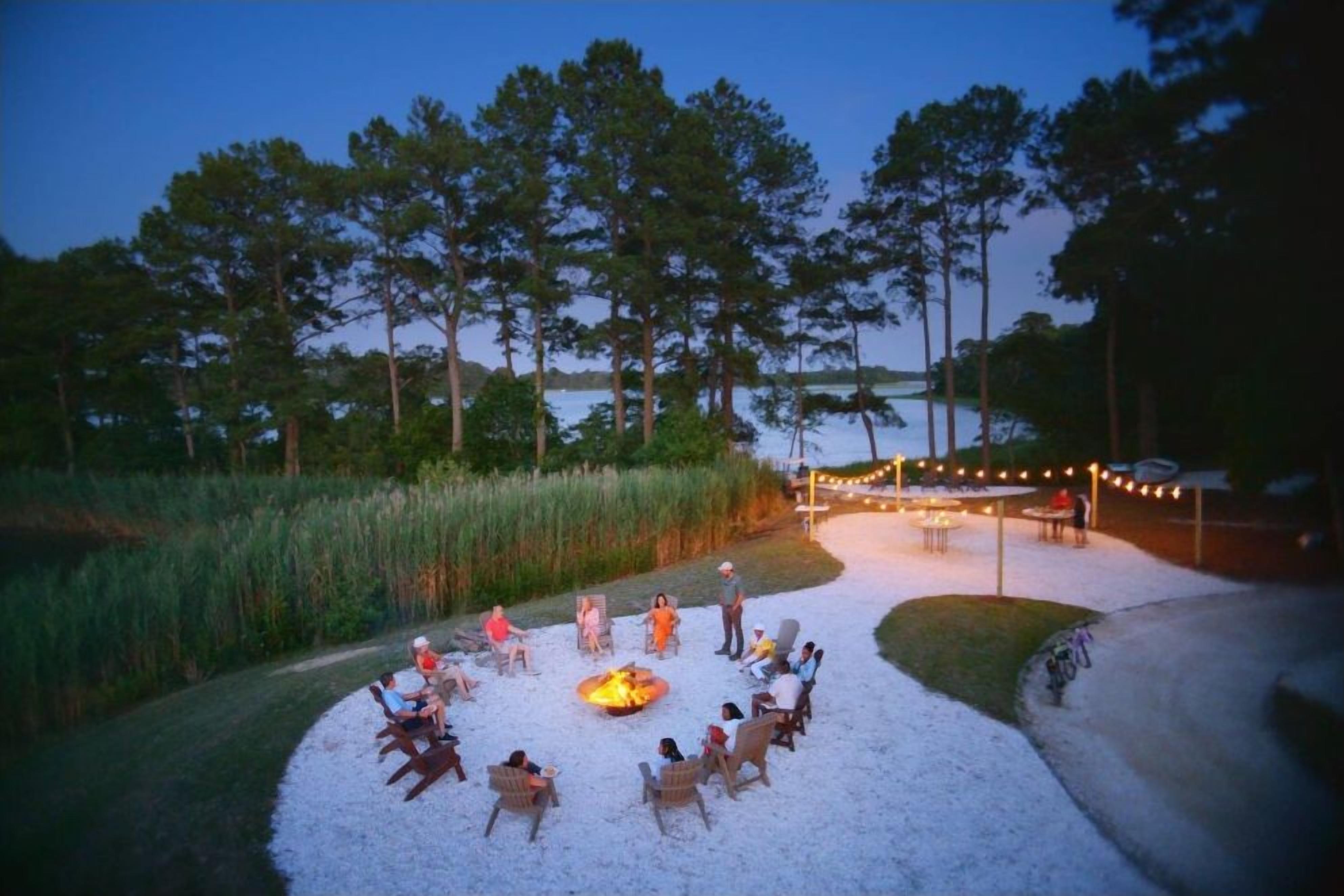 Waterfront fire pit lounge with string lights and serene evening views