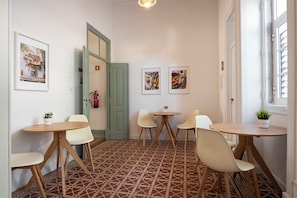 A room with a patterned floor, white walls, and a door leading to another room. There are two round tables with chairs, and two framed pictures on the wall. - Casa Dona Irene Sunny Terrace | Private Room 2 | Faro City Center (Faro)
