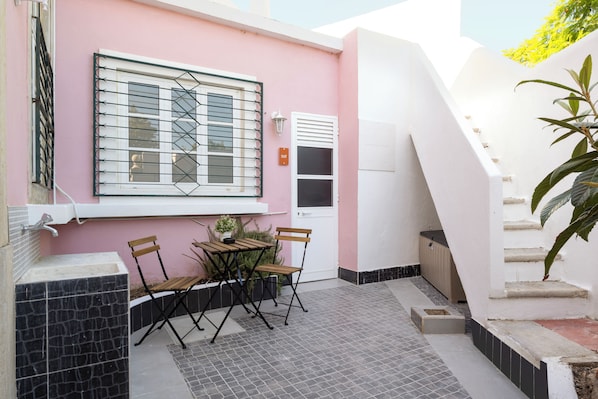 A small outdoor seating area with a table and chairs, a window with metal bars, and a staircase leading to an upper level. - Casa Dona Irene Sunny Terrace | Private Room 2 | Faro City Center (Faro)