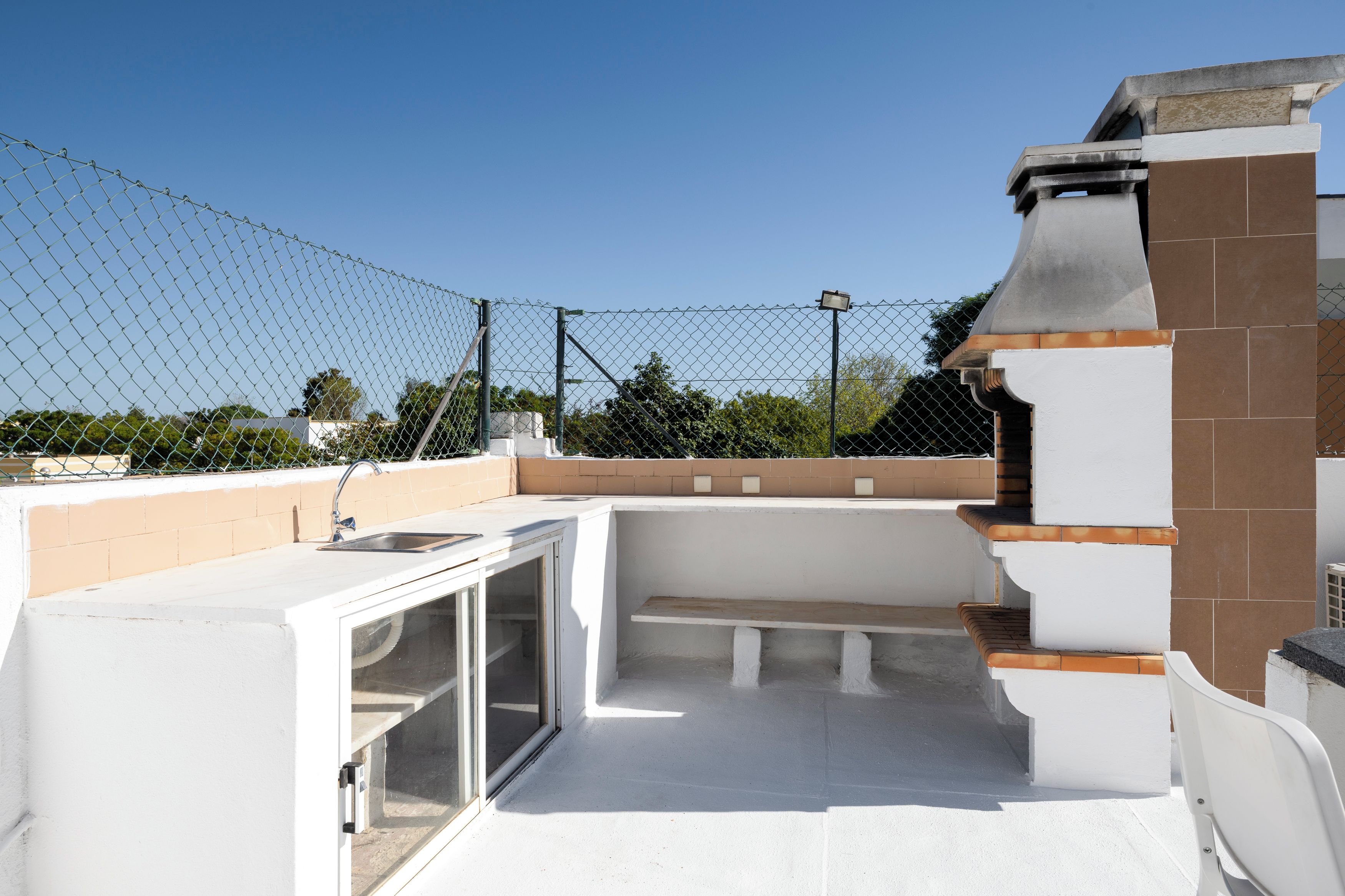 A rooftop patio with a built-in sink, a glass enclosure, and a seating area.