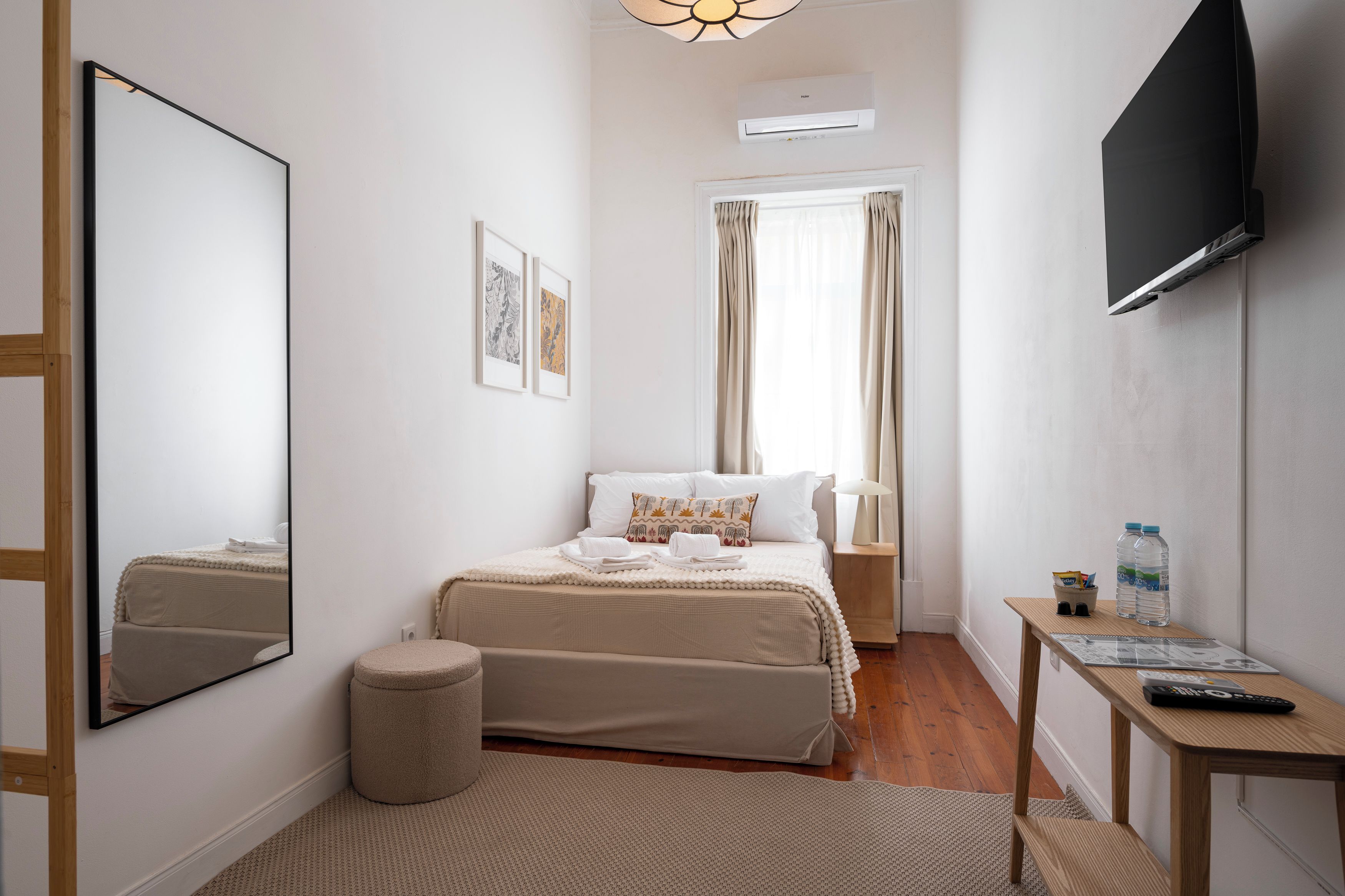 Ein Hotelzimmer mit Bett, Nachttisch, Spiegel, Fernseher und einem Fenster mit Vorhängen.