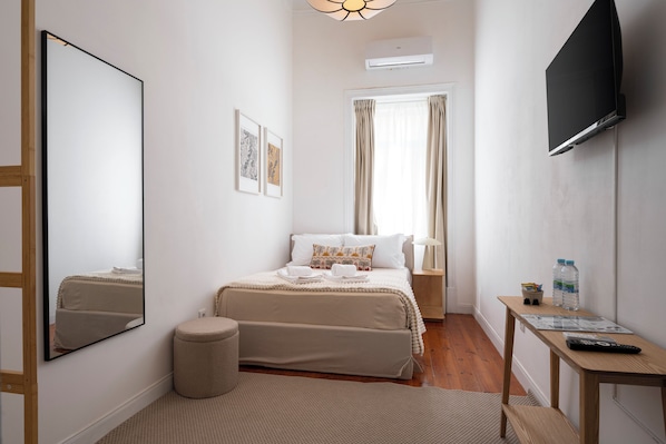 A hotel room with a bed, a bedside table, a mirror, a TV, and a window with curtains.