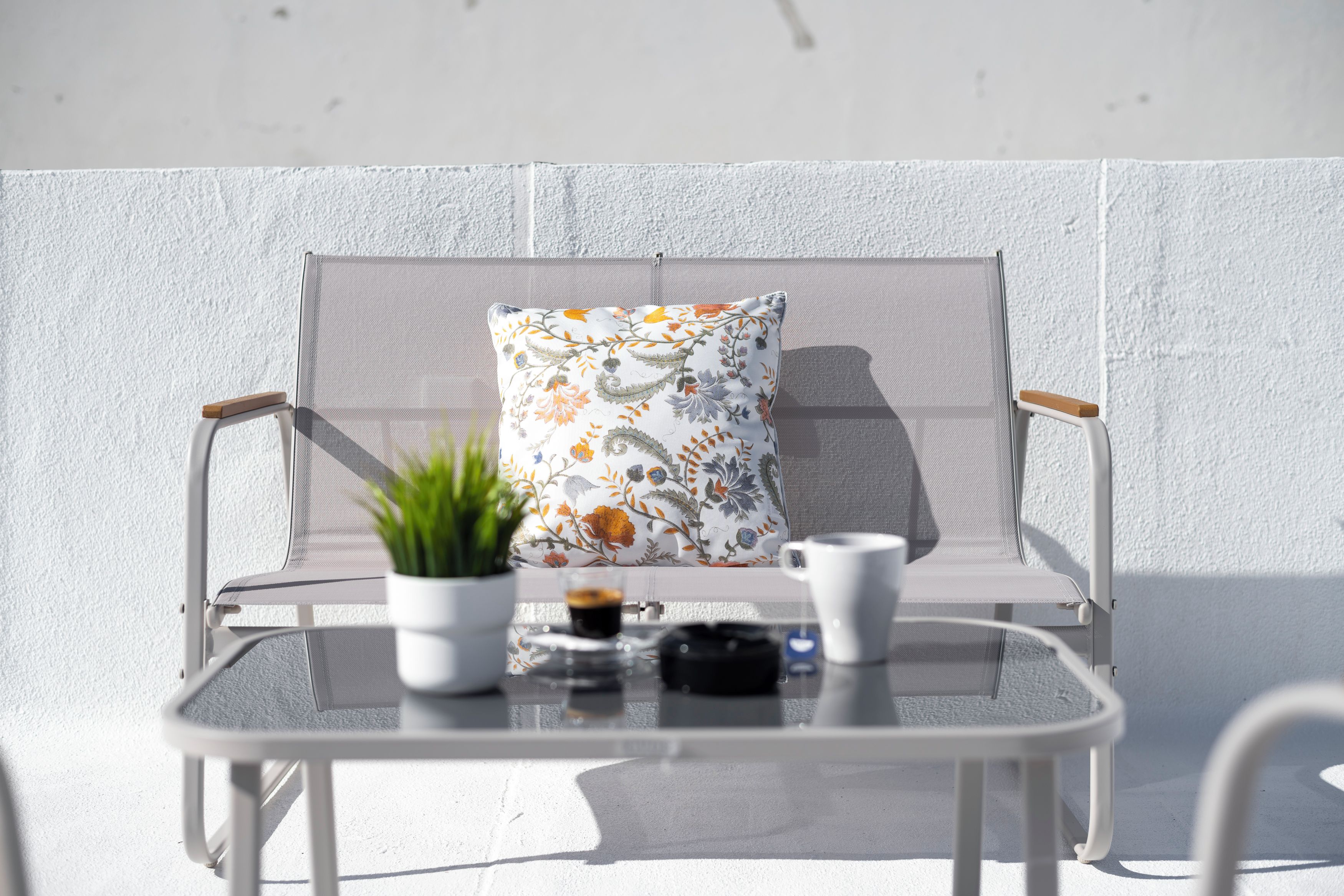 A white outdoor seating area with a cushioned chair, a small table, and a potted plant.