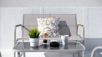 A white outdoor seating area with a cushioned chair, a small table, and a potted plant.