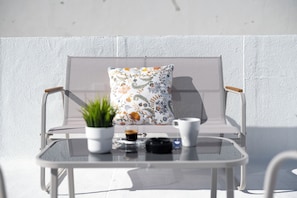 A white outdoor seating area with a cushioned chair, a small table, and a potted plant. - Casa Dona Irene Sunny Terrace | Faro Center | Private Room 3 | Boat Marina (Faro)
