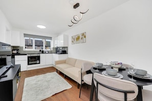 Una cocina moderna con armarios blancos, un sofá beige y una mesa de comedor preparada para cuatro personas.