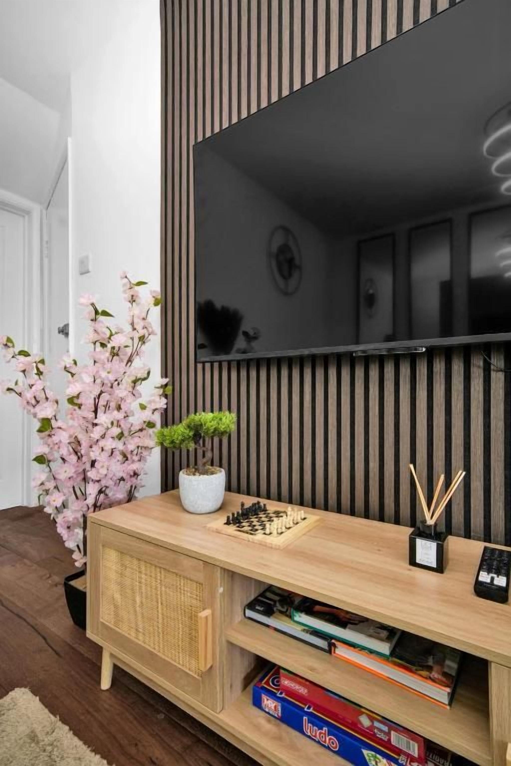 Una sala de estar moderna con un mueble de madera para entretenimiento, un televisor montado en la pared y una pequeña planta en maceta.
