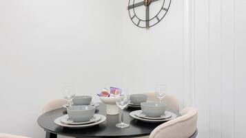 Una mesa de comedor dispuesta con fuentes, platos y vasos, con un reloj de pared encima.