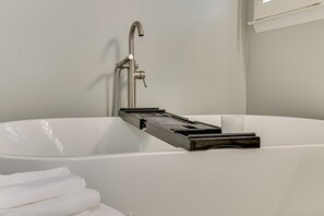 A modern bathroom with a freestanding bathtub, a handheld showerhead, and a towel rack. - Quaint 4-bedroom house with pool in charming Evans (Evans)