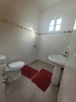 Un baño con inodoro, bidé y lavamanos, paredes con azulejos y una ventana.