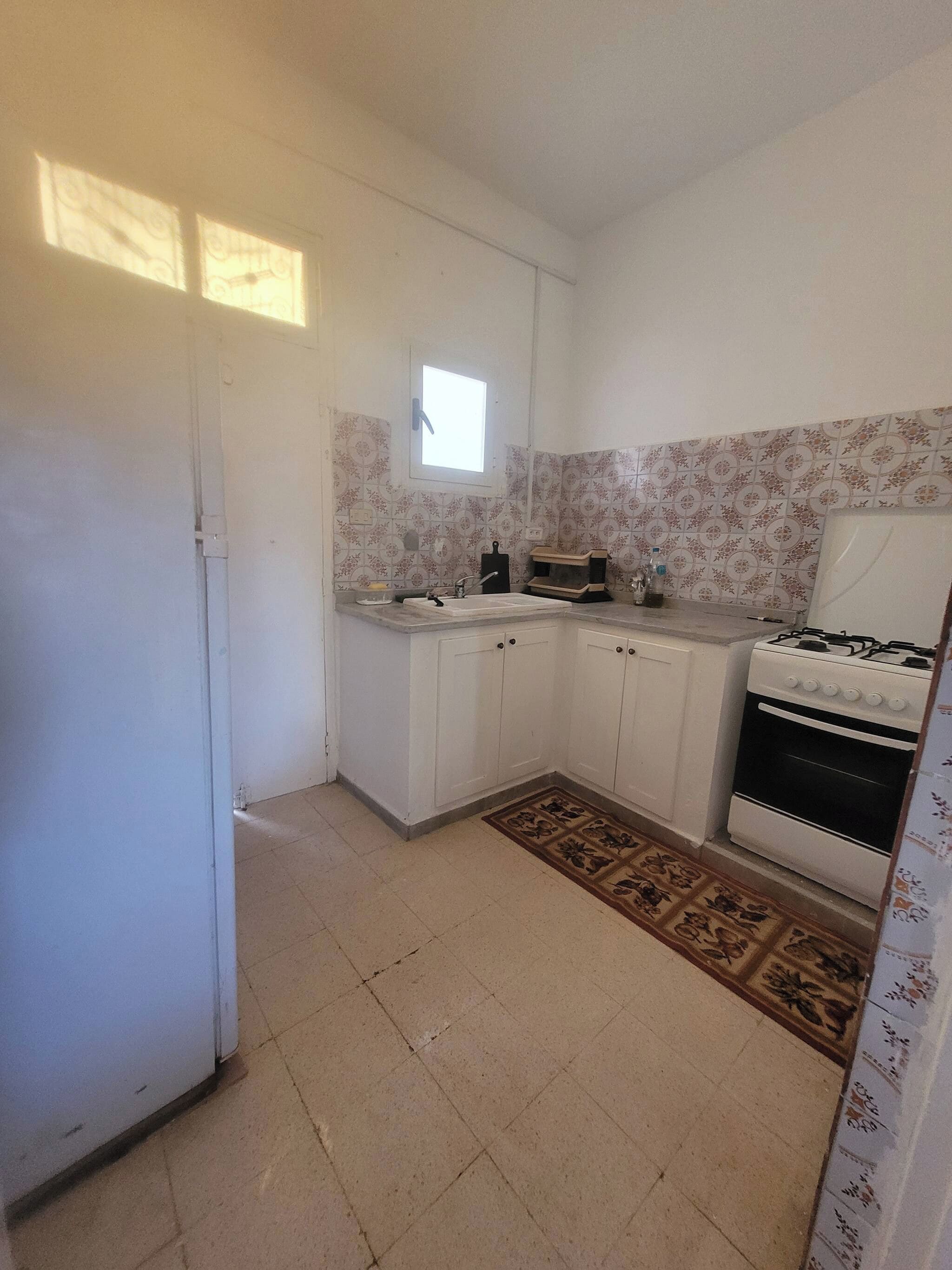 Cocina compacta con armarios blancos, estufa a gas, microondas y un ventanal.