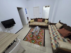 A living room with a sofa, a television, a coffee table, and a patterned rug. - The Djerbien Houmet Souk (Houmt Souk)