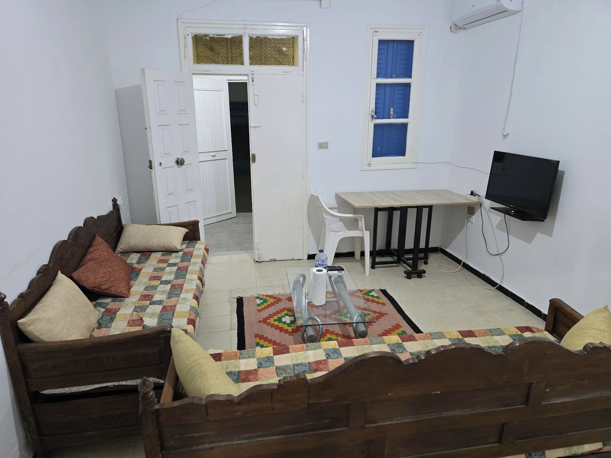 Una habitación con un sofá de madera, una mesita, un televisor y una puerta que da a otra habitación.