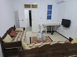 A room with a wooden sofa, a small table, a TV, and a door leading to another room. - The Djerbien Houmet Souk (Houmt Souk)