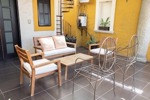 A cozy outdoor seating area with a sofa, two chairs, and a table, surrounded by yellow walls and a tiled floor. - Oaxacan house with a terrace (Oaxaca de Juárez)