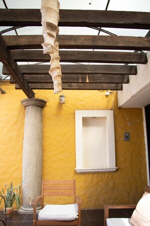 A covered patio area with a wooden bench, a stone column, and a white window. - Oaxacan house with a terrace (Oaxaca de Juárez)