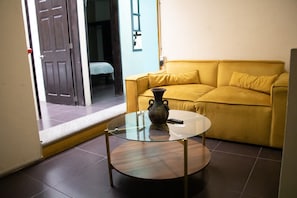 A room with a yellow sofa, a glass coffee table with a vase, and a door leading to another room. - Oaxacan house with a terrace (Oaxaca de Juárez)