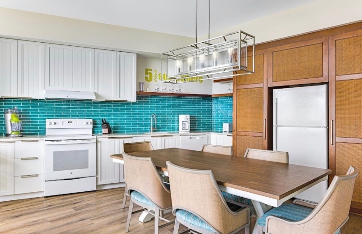A modern kitchen with white cabinets, a wooden dining table, and teal backsplash.