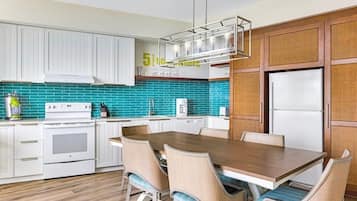 A modern kitchen with white cabinets, a wooden dining table, and teal backsplash.