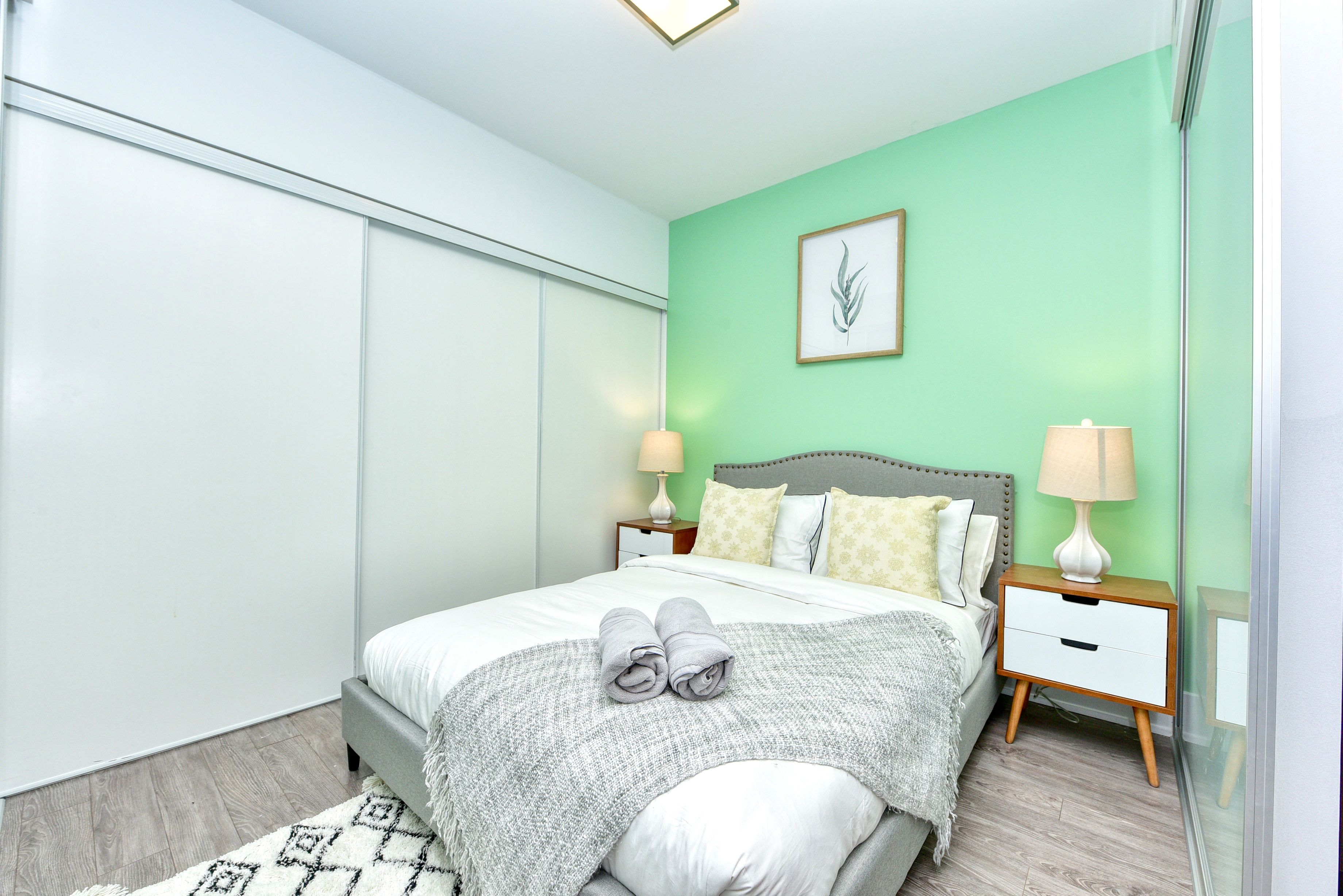 A modern bedroom with a bed, nightstands, and a wall-mounted lamp.