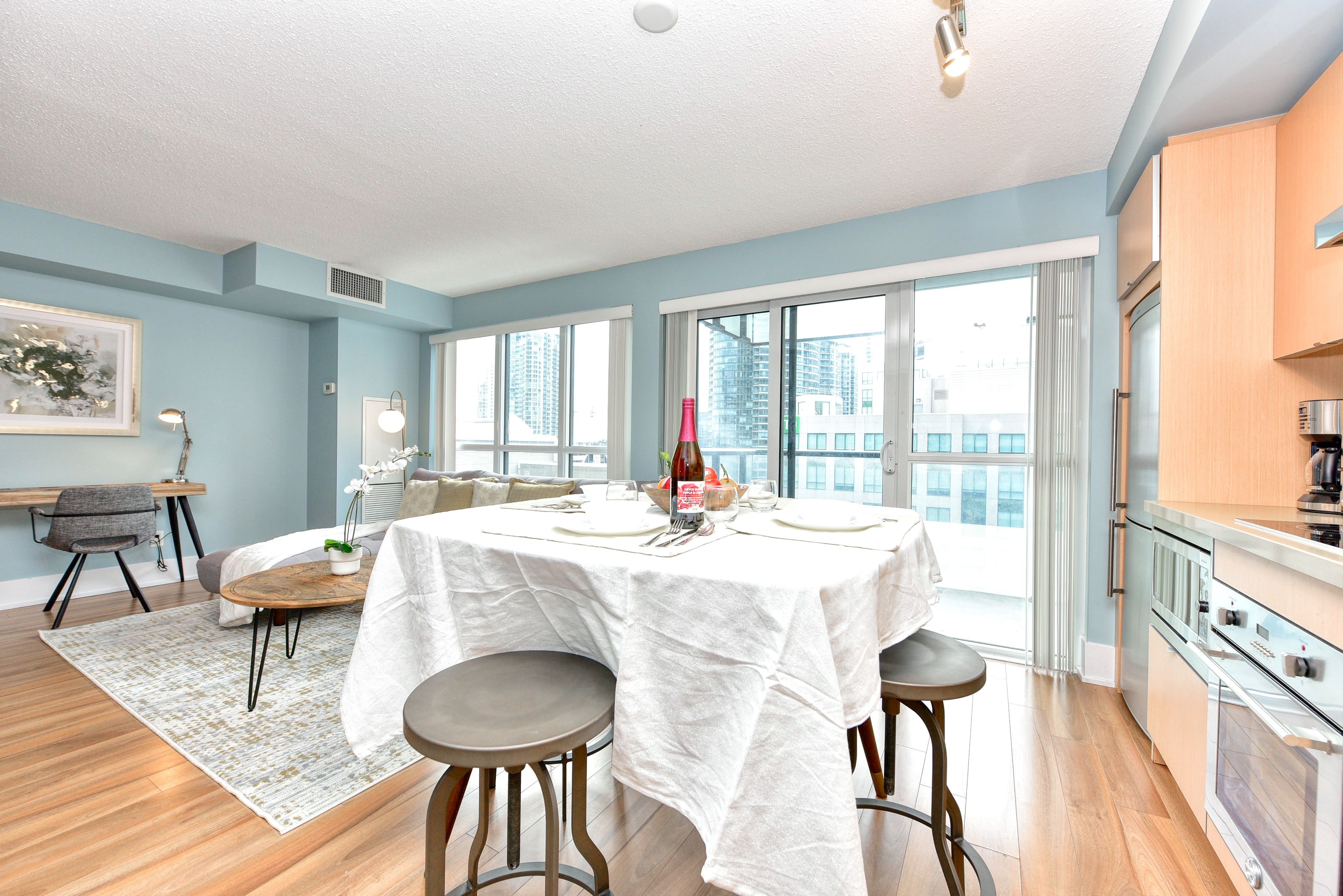 A modern kitchen with a dining area, large windows, and a view of the city.
