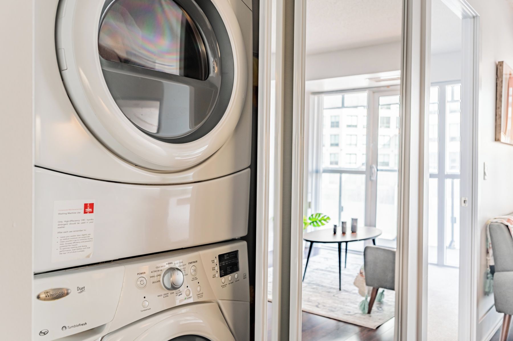 Lavadora y secadora Whirlpool Duet de carga frontal apiladas en un apartamento moderno, con vista a un comedor y grandes ventanales.