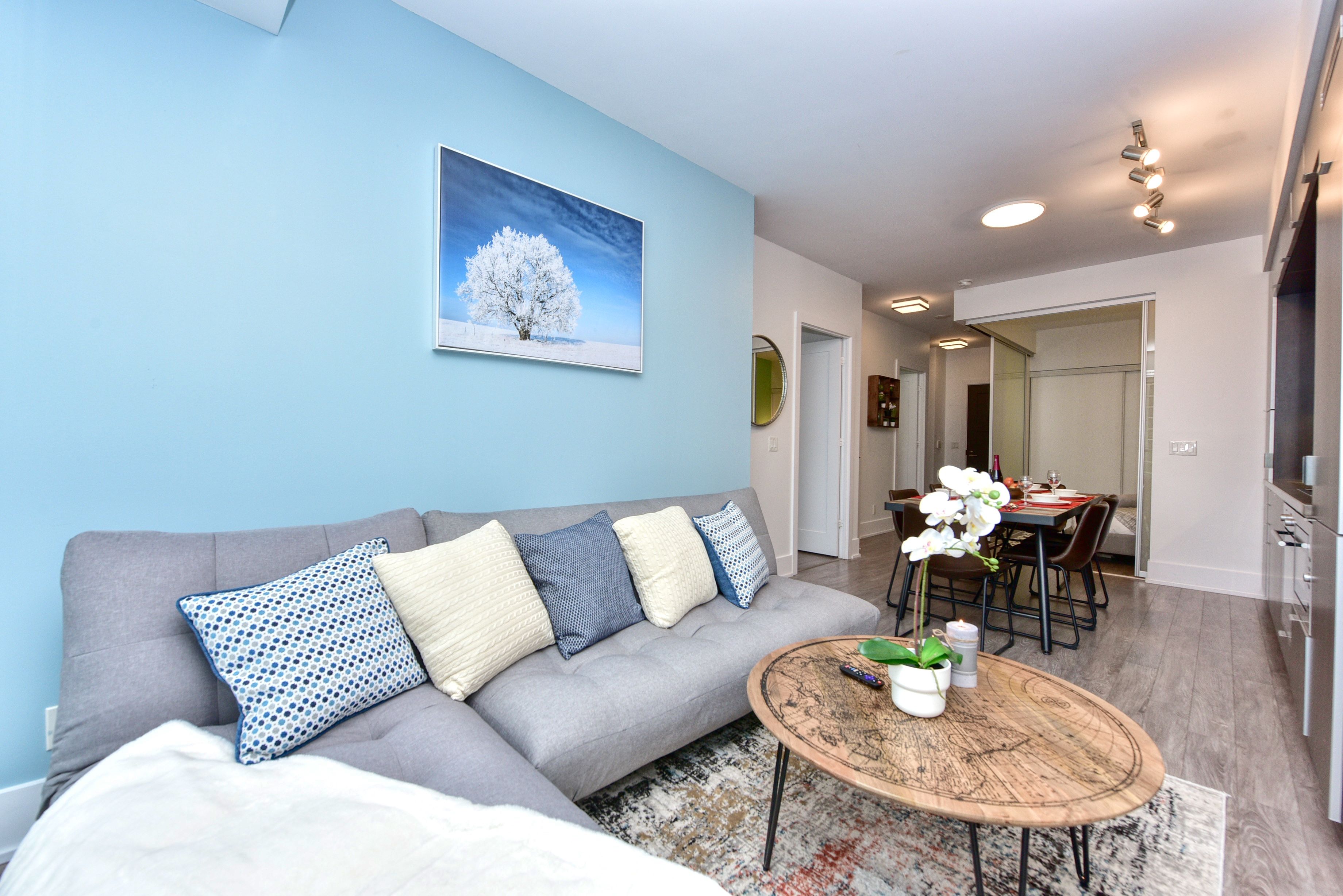A modern living room with a grey sofa, a coffee table, and a dining area with a table and chairs.
