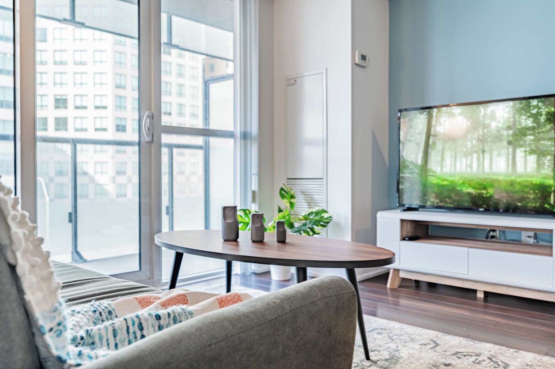 A modern living room with a sofa, a coffee table, a TV, and a large window with a view of buildings.
