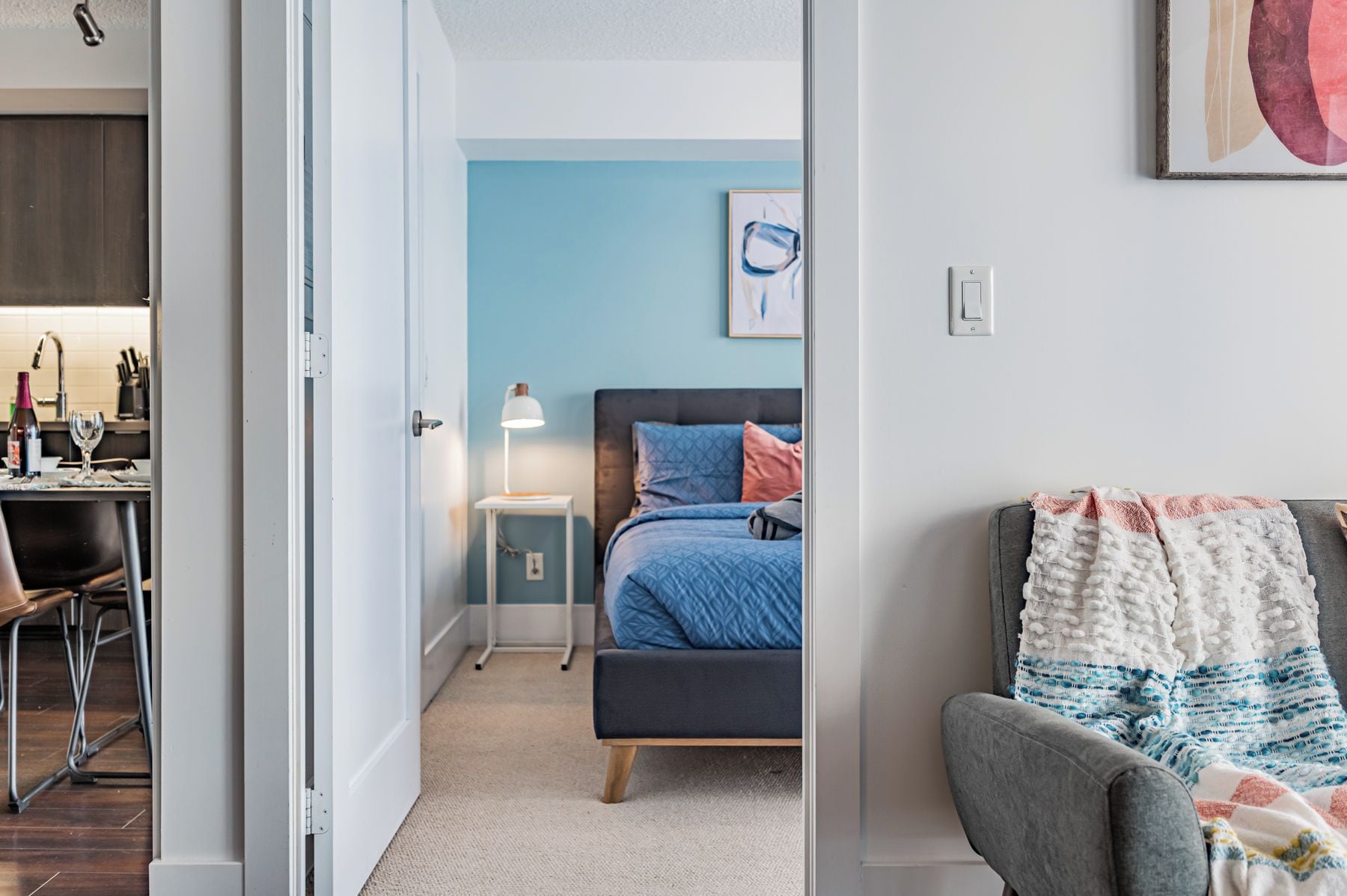 Quarto com cama, mesa de cabeceira, luminária e um quadro na parede.