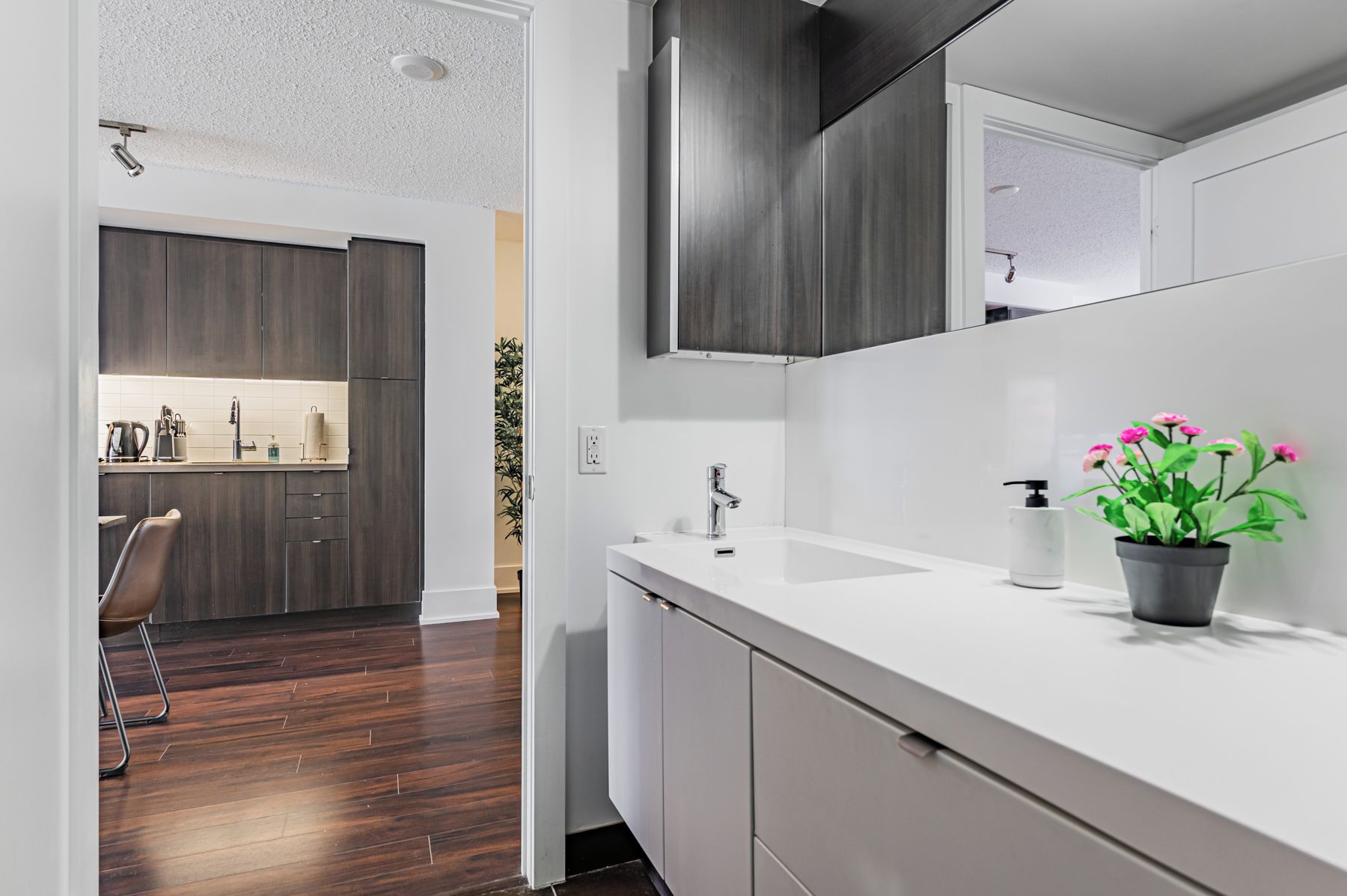 Un baño moderno con un lavamanos blanco, un espejo y una planta en maceta con flores rosadas.
