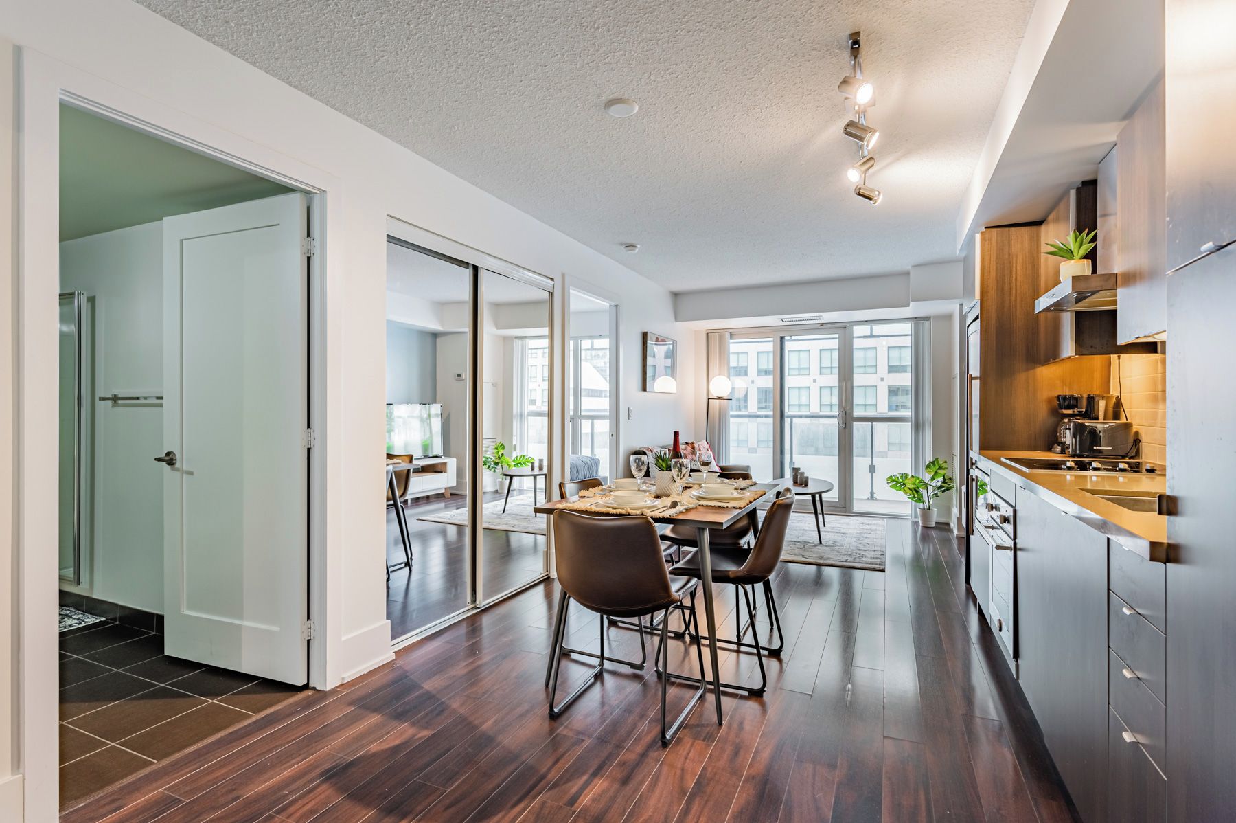 Una cocina moderna con electrodomésticos de acero inoxidable, un comedor con mesa y sillas de madera, y vistas de la ciudad a través de amplios ventanales.