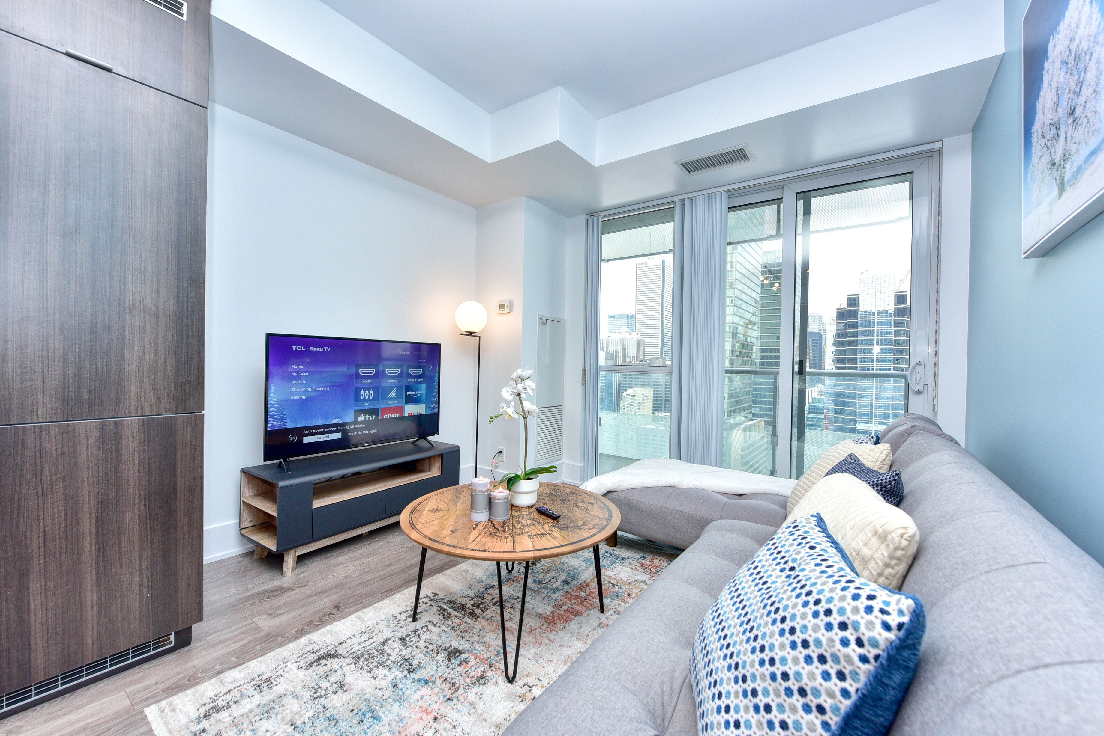 A modern living room with a grey sofa, a round coffee table, and a flat-screen TV on a wooden stand.