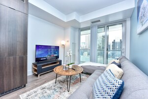Una sala de estar moderna con un sofá gris, una mesa de centro redonda y un televisor de pantalla plana sobre un soporte de madera.