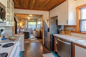 A compact kitchen with a refrigerator, stove, and wooden cabinets. - Cannon Beach Cottage – Walk to Beach & Downtown, Fenced Yard + Dog Friendly (Cannon Beach)