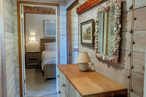 Ein Schlafzimmer mit einem hölzernen Kopfende, einer Nachttischlampe, einem gerahmten Bild an der Wand und einem Spiegel mit Muscheldekoration.