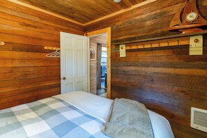 A wooden-paneled room with a bed, a door, a coat rack, and a wall-mounted clock. - Cannon Beach Cottage – Walk to Beach & Downtown, Fenced Yard + Dog Friendly (Cannon Beach)