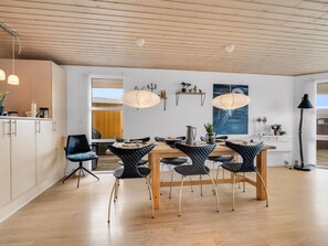 A modern dining area with a wooden table and black chairs, a kitchen area with white cabinets, and a large window providing natural light. - "Aarthi" - 300m from the sea by Interhome (Harboøre)